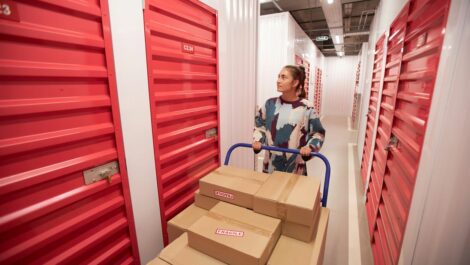 A young woman pushing a handcart with boxes in a storage facility.